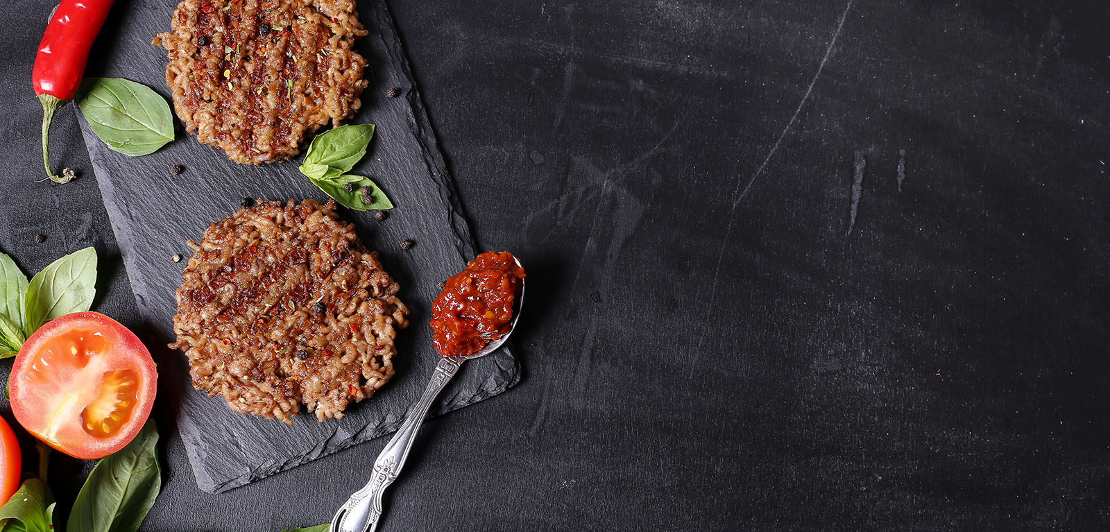 Zwei gebratene Frikadellen auf Schieferplatte mit Tomaten und Salat