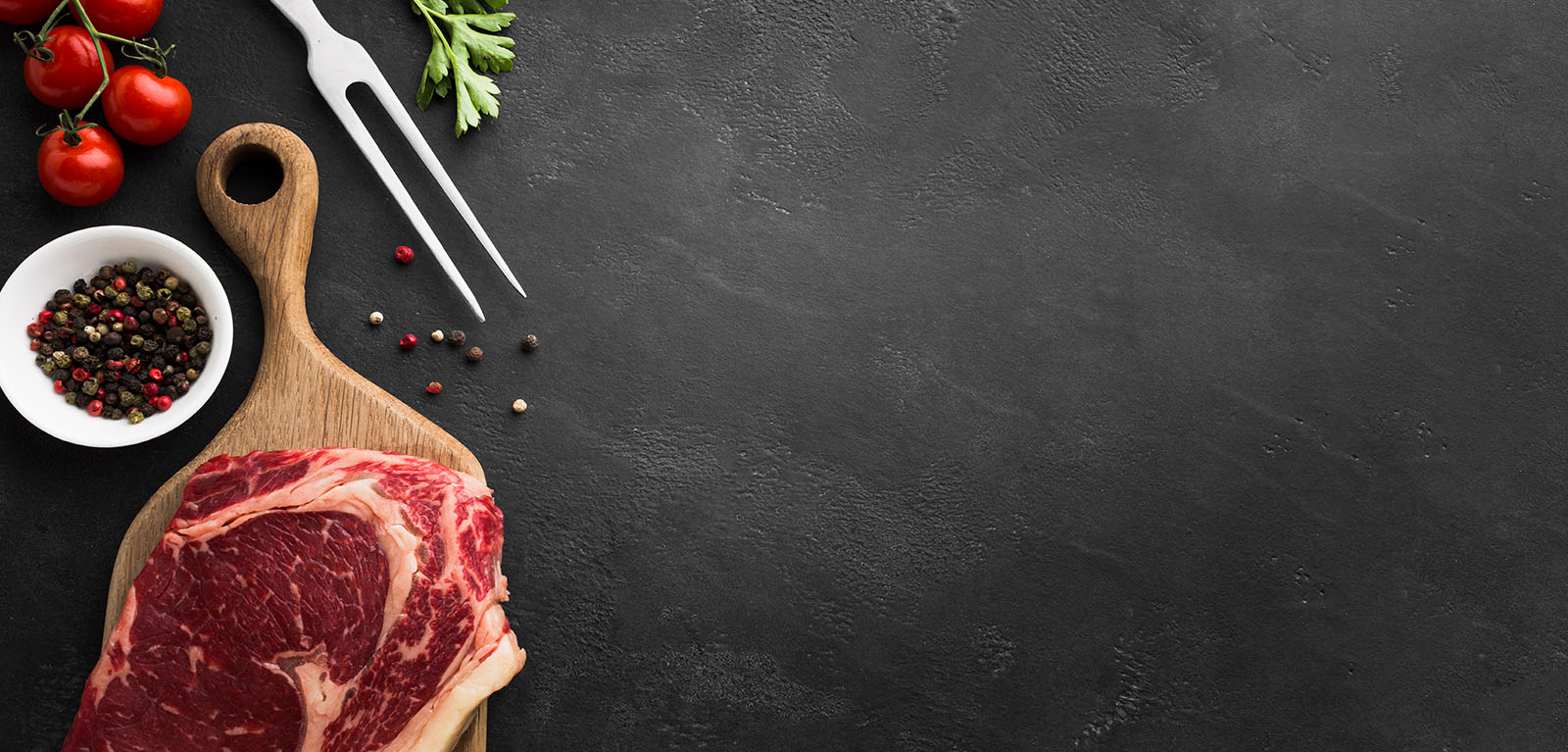 Rohes rotes Fleisch auf Holzbrett mit Pfefferschale und Spießgabel
