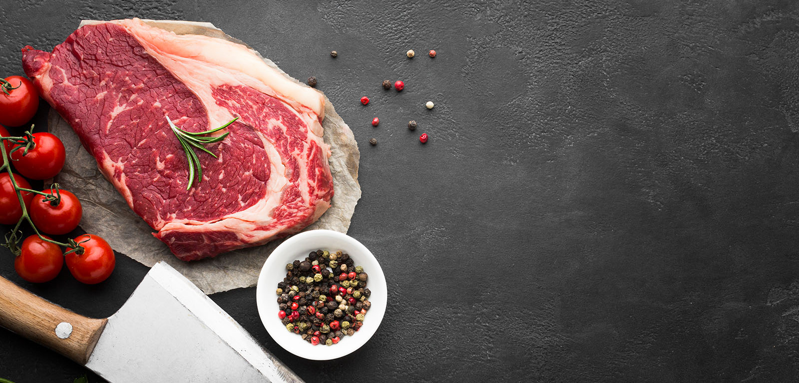 Rohes Fleisch auf dunklem Untergrund mit Messer und Schälchen mit Pfeffer